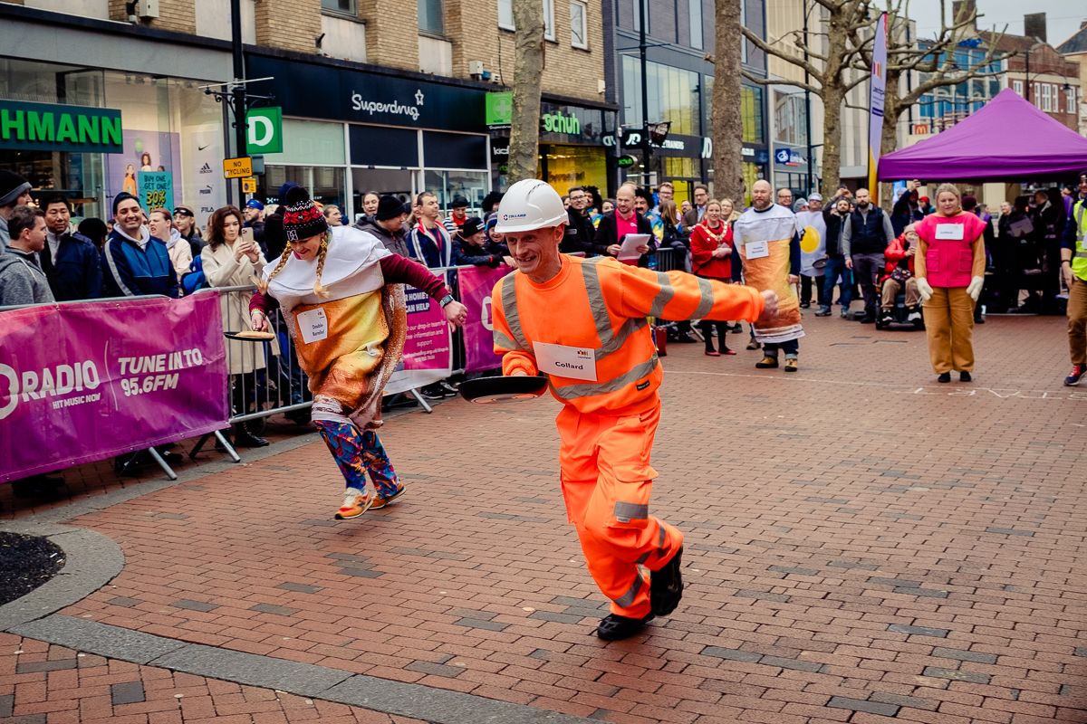 A man and a woman racing with frying pans, part of Reading Pancake race on Broad Street